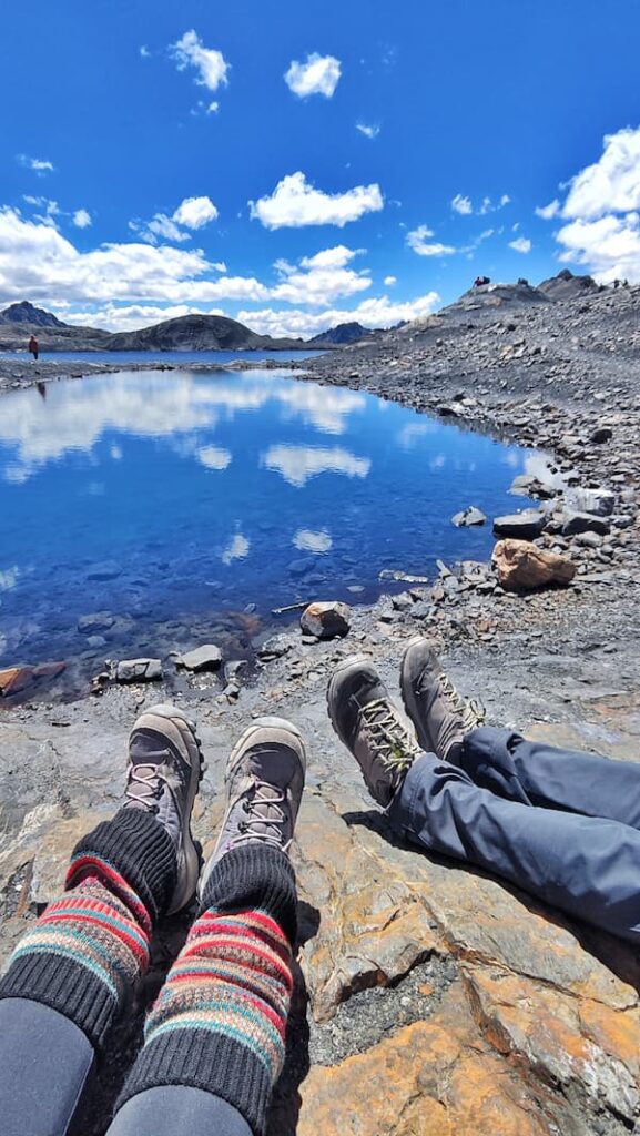 Pies de dos personas junto a una laguna de alta montaña con el glaciar del Nevado Pastoruri al fondo